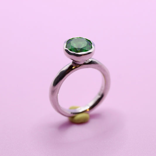 Silver ring with a tsavorite green gemstone on a pink background