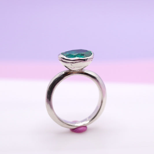 Silver ring with a paraiba green gemstone on a gradient pink and purple background