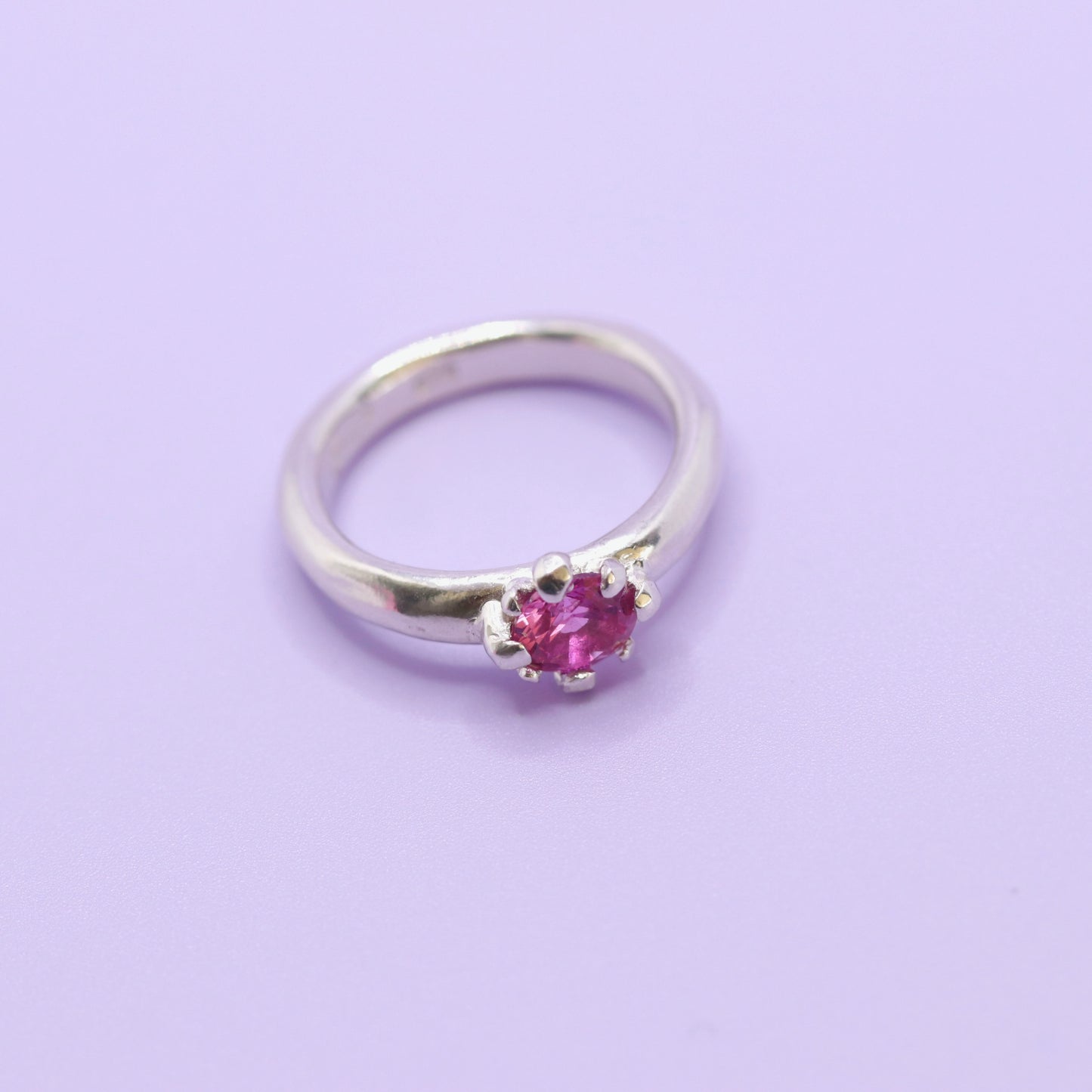 Silver ring with a pink gemstone on a light purple background