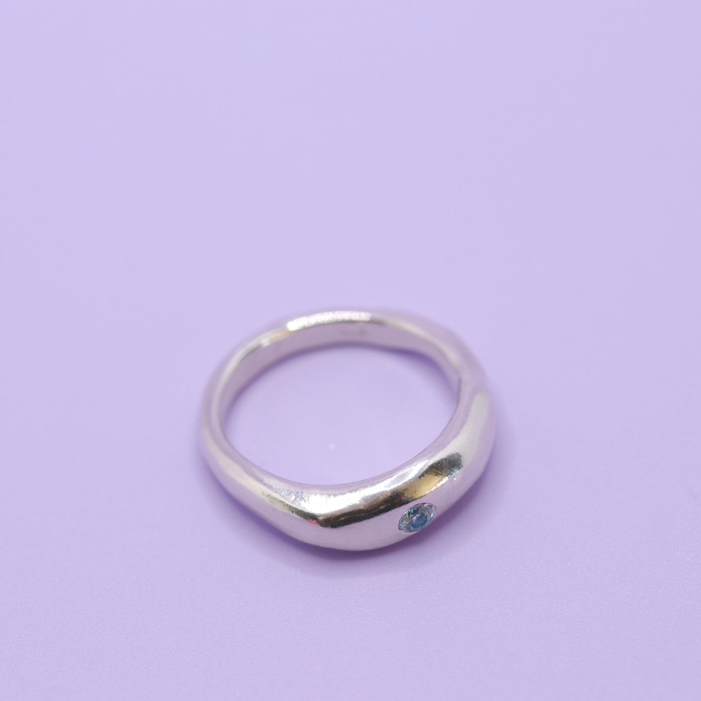 Silver ring with a blue gemstone on a light purple background