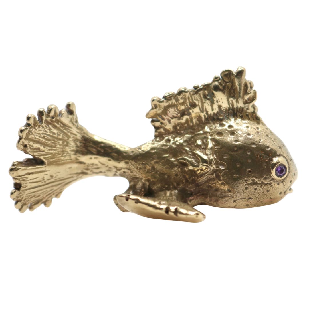 Gold fish-shaped object with a purple gemstone eyes on a white background