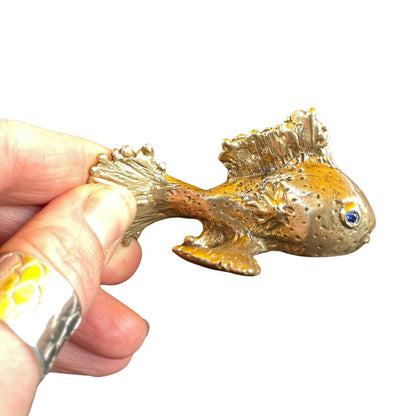 Hand holding a gold fish object against a white background