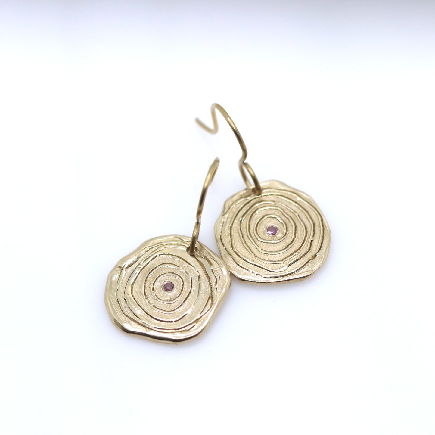 Gold circular earrings with a central gemstone on a white background