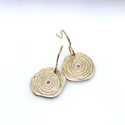 Gold circular earrings with a central gemstone on a white background