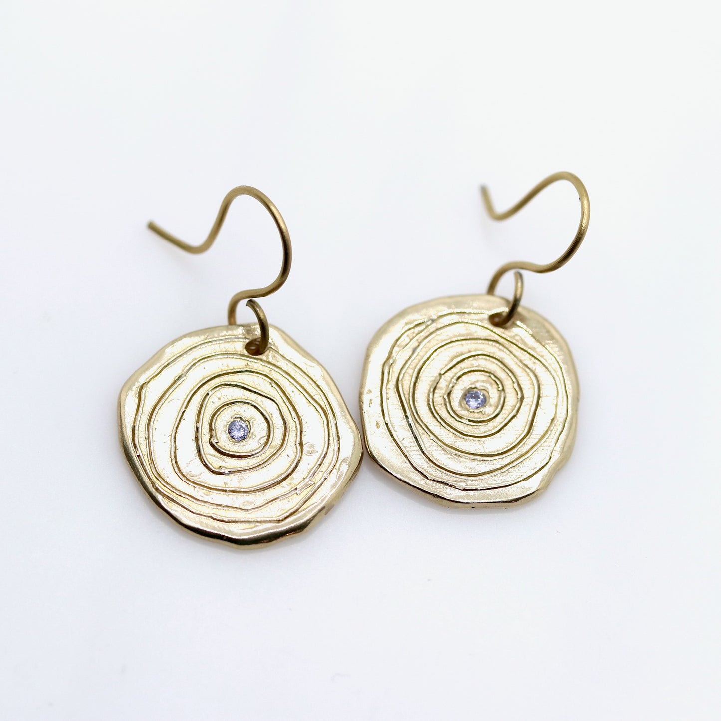 Gold circular earrings with a central gemstone on a white background