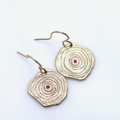 Gold circular earrings with a central red gemstone on a white background