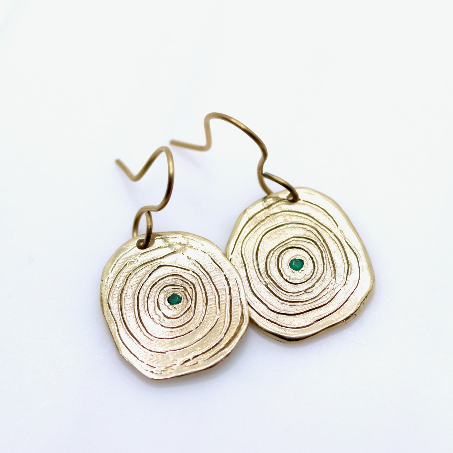 Gold circular earrings with green stones on a white background