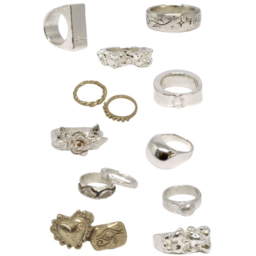 A collection of ten silver and bronze rings arranged on a plain white background, featuring various designs including floral, heart, and textured bands.