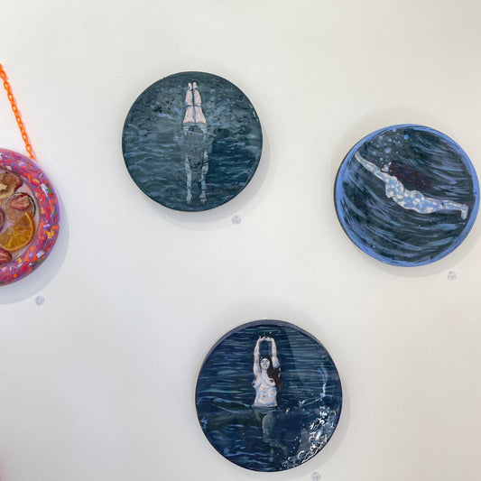 Four circular artworks on a white background, featuring artistic depictions of people in water.