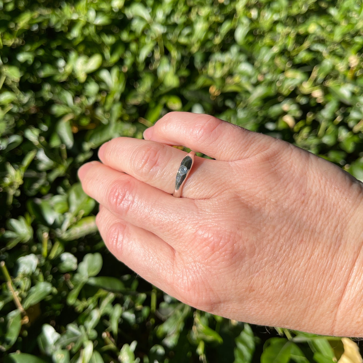 Hand wearing a ring with a green bush background