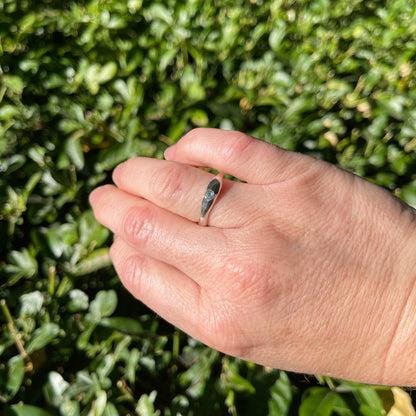 Hand wearing a ring with a green bush background