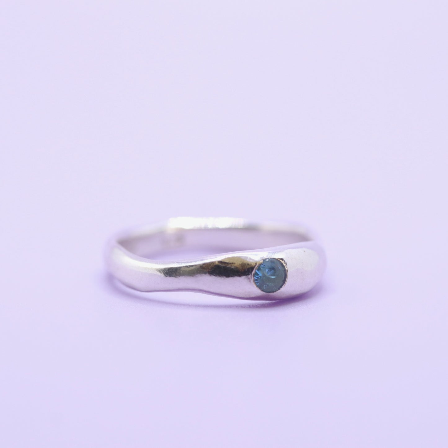 Silver ring with a blue gemstone on a light purple background