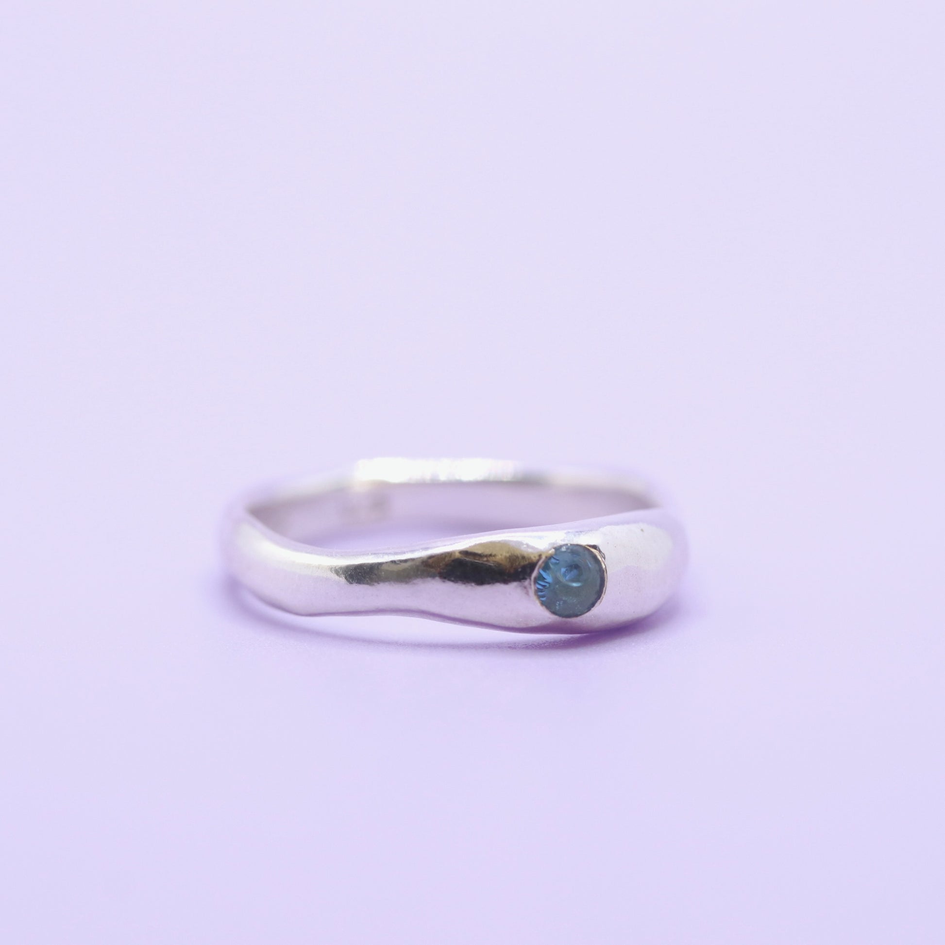 Silver ring with a blue gemstone on a light purple background