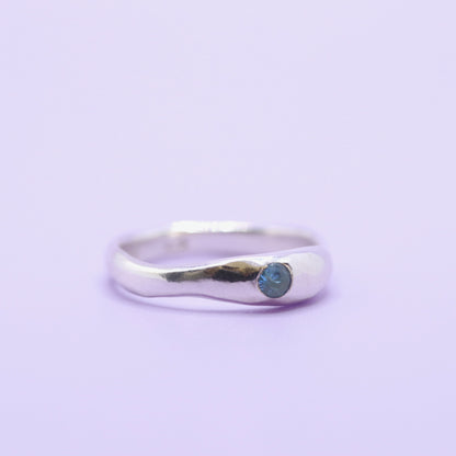 Silver ring with a blue gemstone on a light purple background