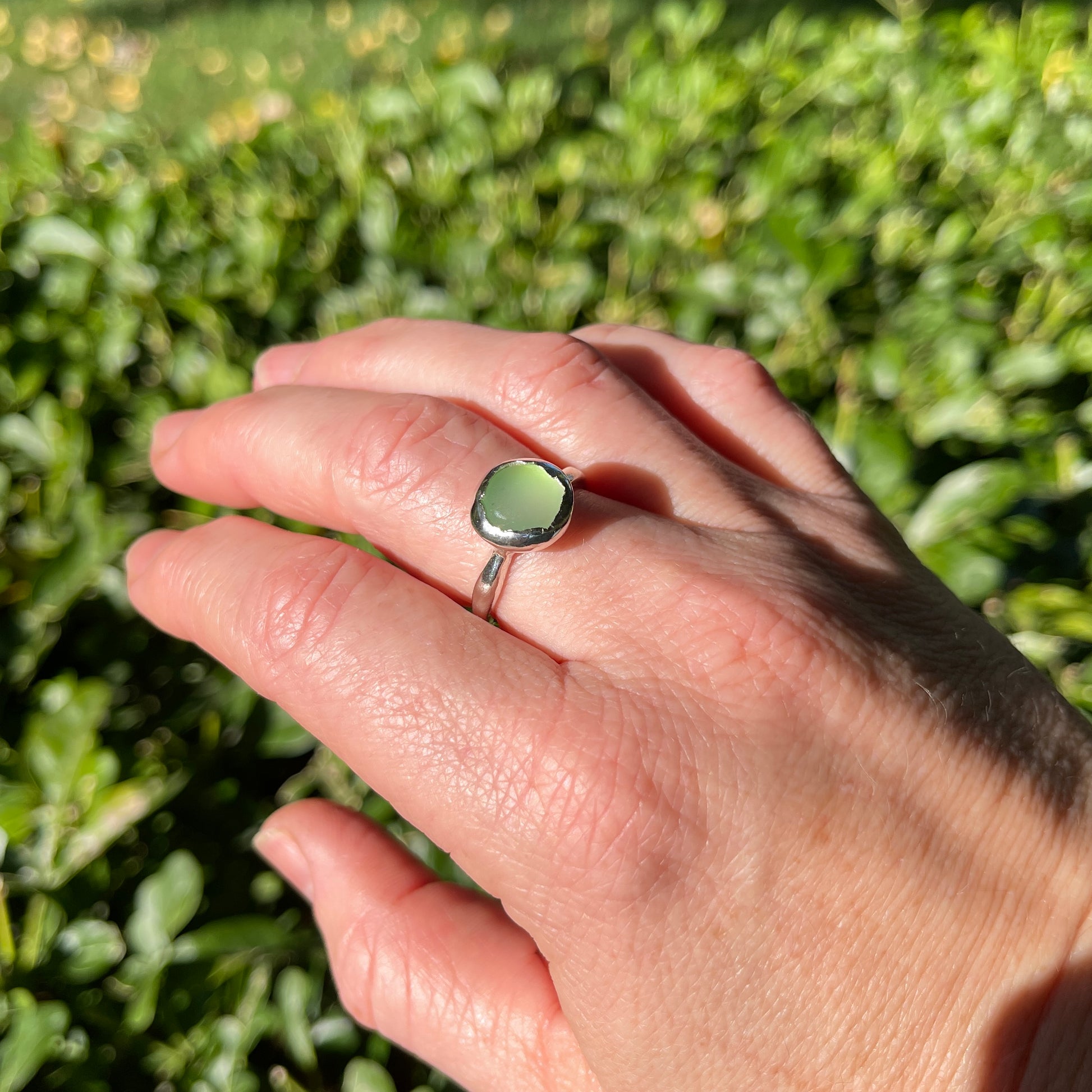 Hand wearing a green ring with a blurred green background