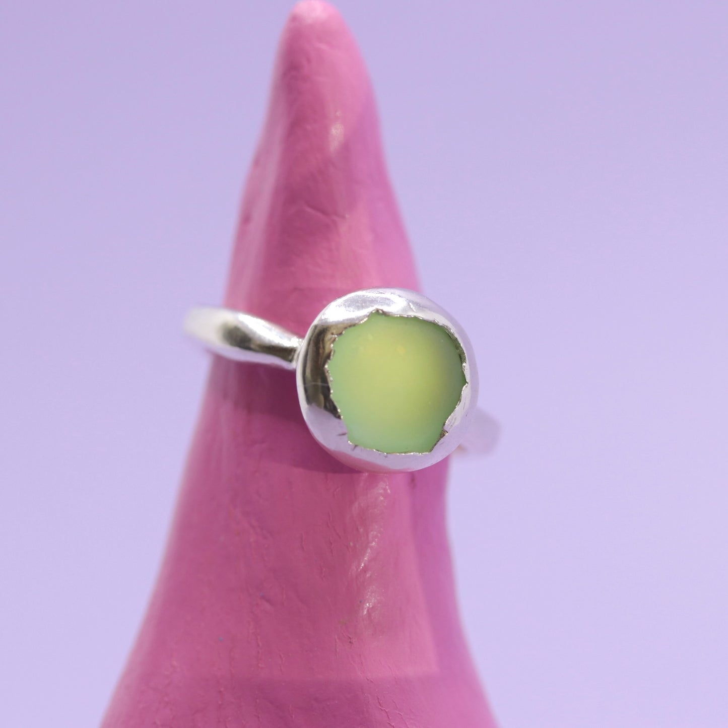 Silver ring with a green stone on a pink finger against a purple background