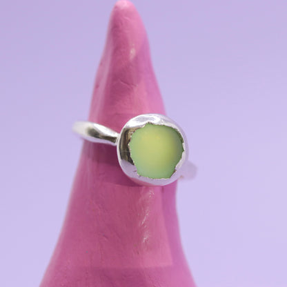 Silver ring with a green stone on a pink finger against a purple background