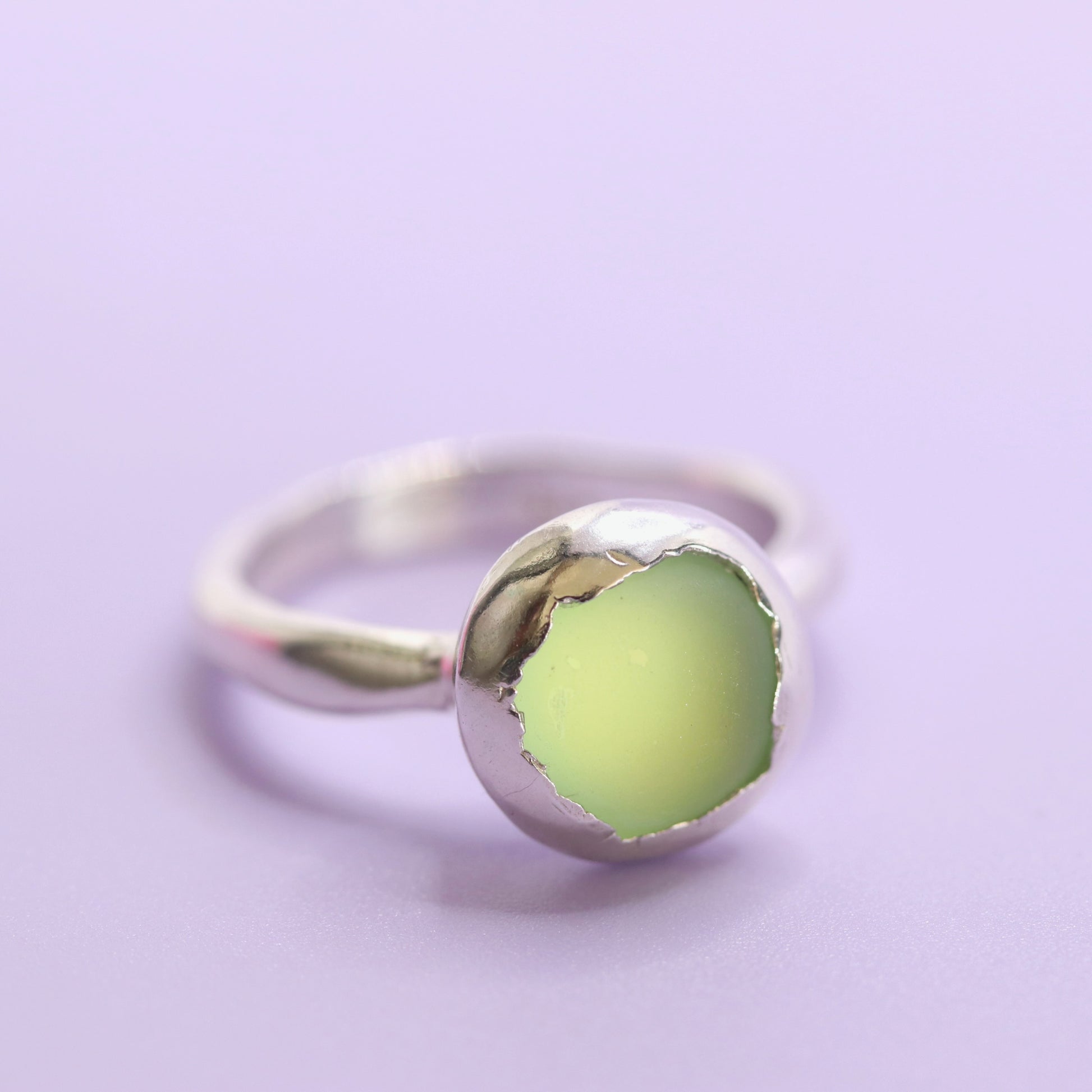 Silver ring with a green stone on a light purple background