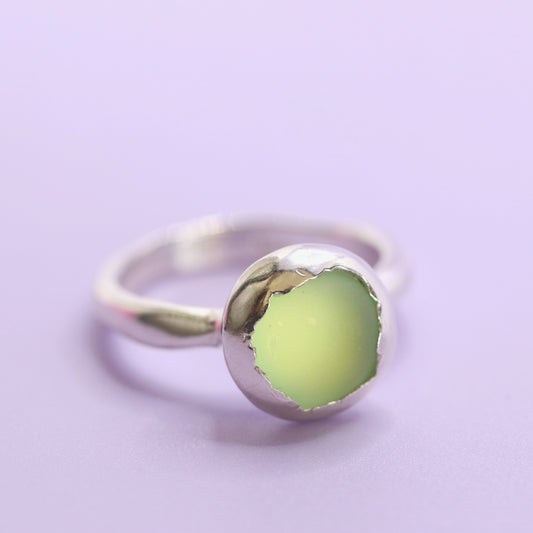 Silver ring with a green stone on a light purple background