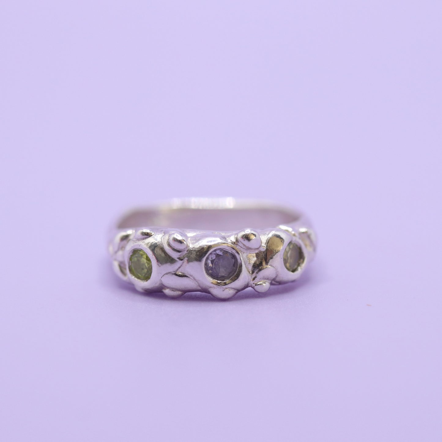 Silver ring with two green and one lavender gem on purple background