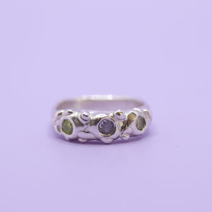 Silver ring with two green and one lavender gem on purple background