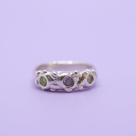 Silver ring with two green and one lavender gem on purple background