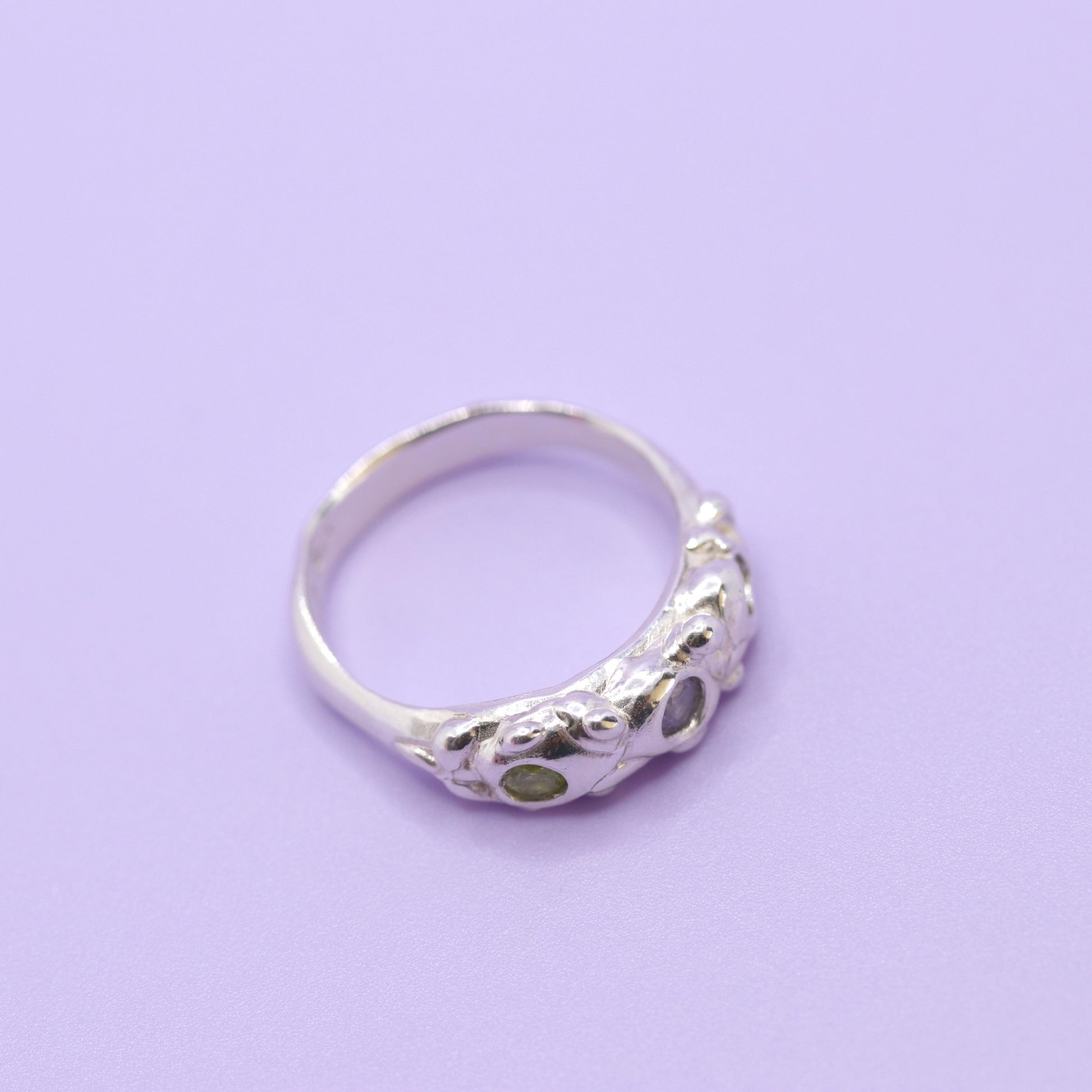 Silver ring with a green stone on a purple background