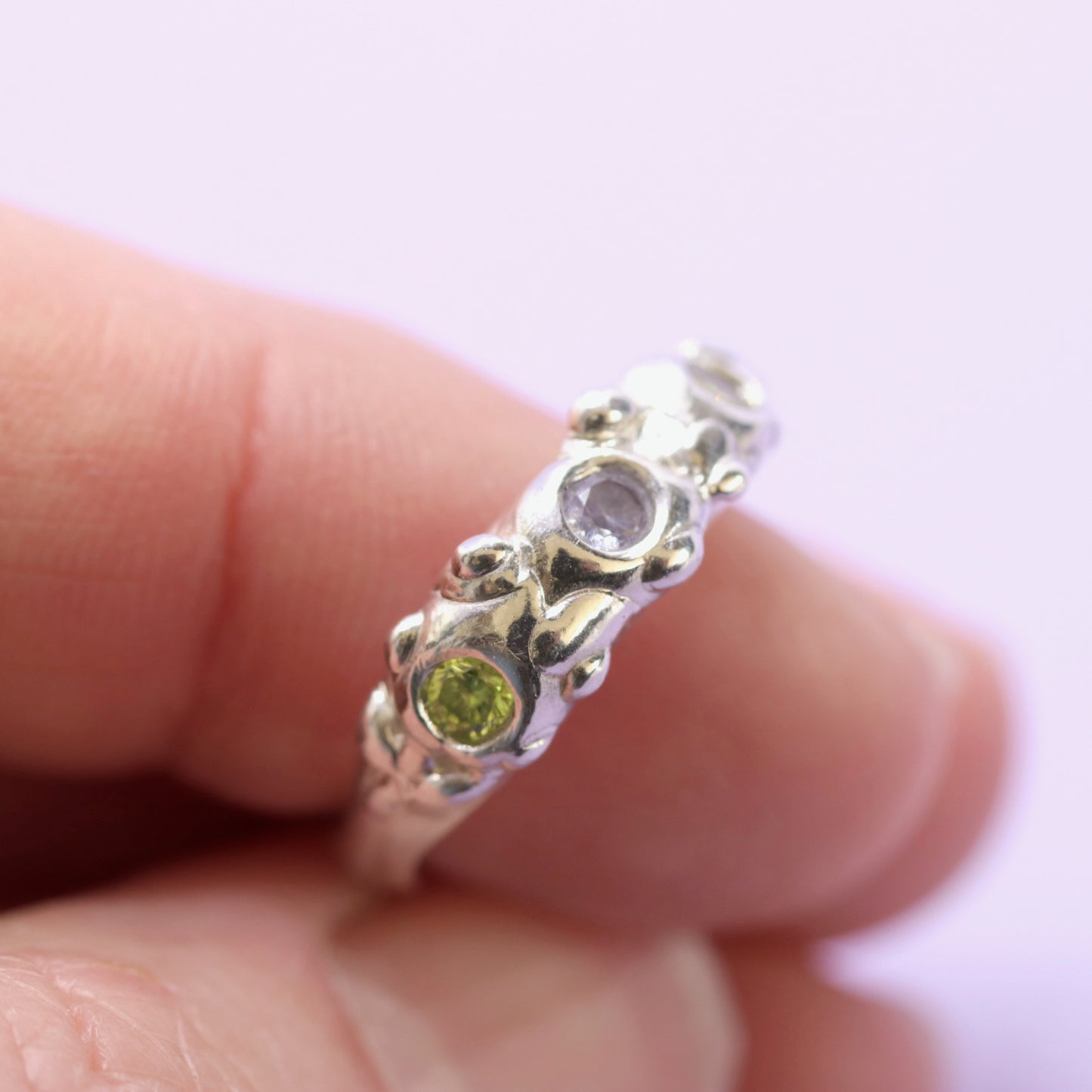 Silver ring with green and purple gemstone on a finger against a white background