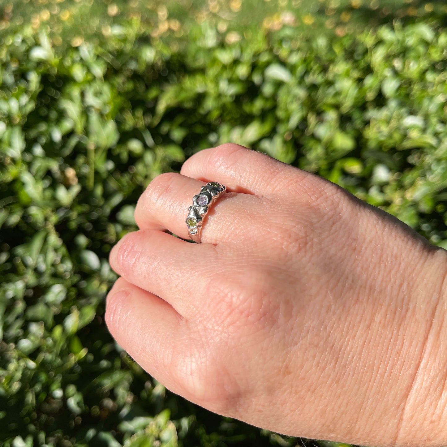 Hand wearing a ring with green gemstones against a blurred green background