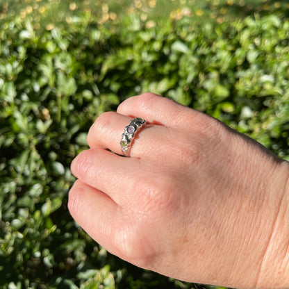 Hand wearing a ring with green gemstones against a blurred green background
