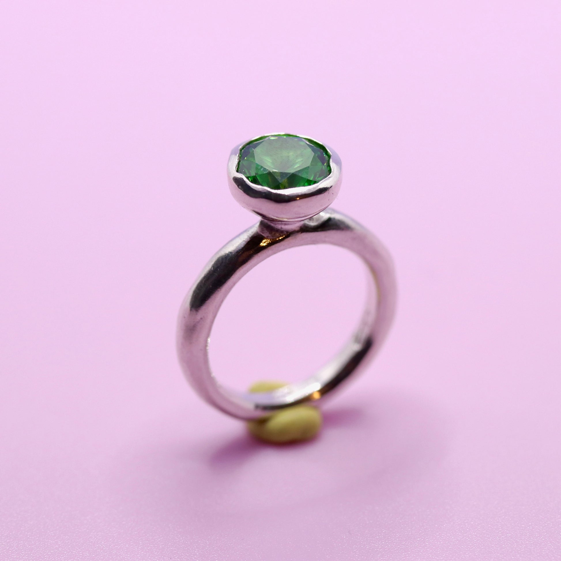 Silver ring with a tsavorite green gemstone on a pink background