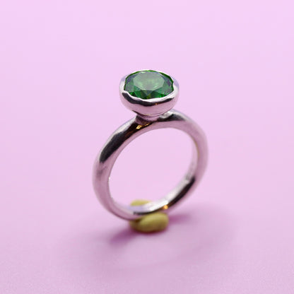 Silver ring with a tsavorite green gemstone on a pink background
