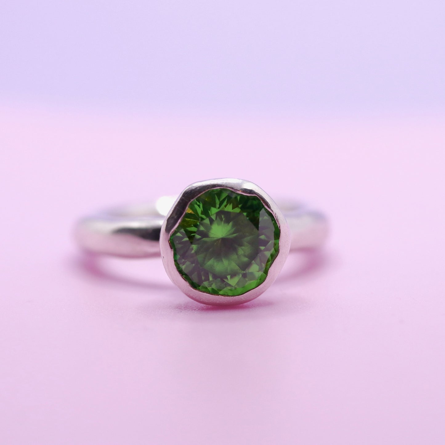 Silver ring with a tsavorite green gemstone on a pink background. New Zealand made jewellery designer