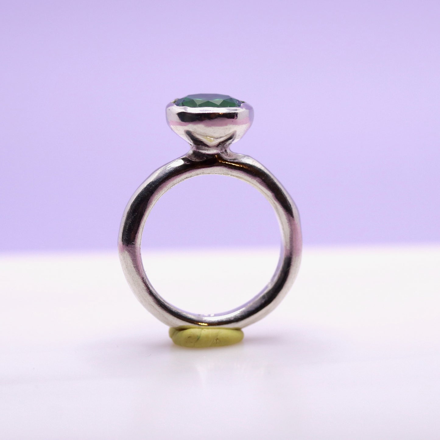 Silver ring with a tsavorite green gemstone on a white surface with a purple background. New Zealand made jewellery designer