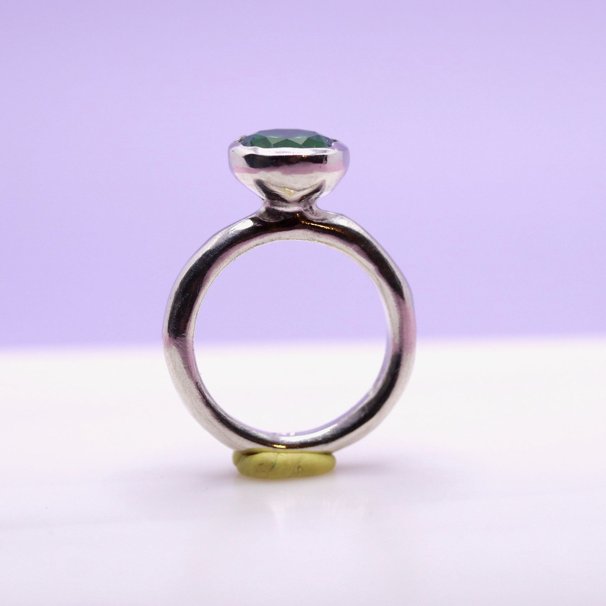 Silver ring with a tsavorite green gemstone on a white surface with a purple background. New Zealand made jewellery designer