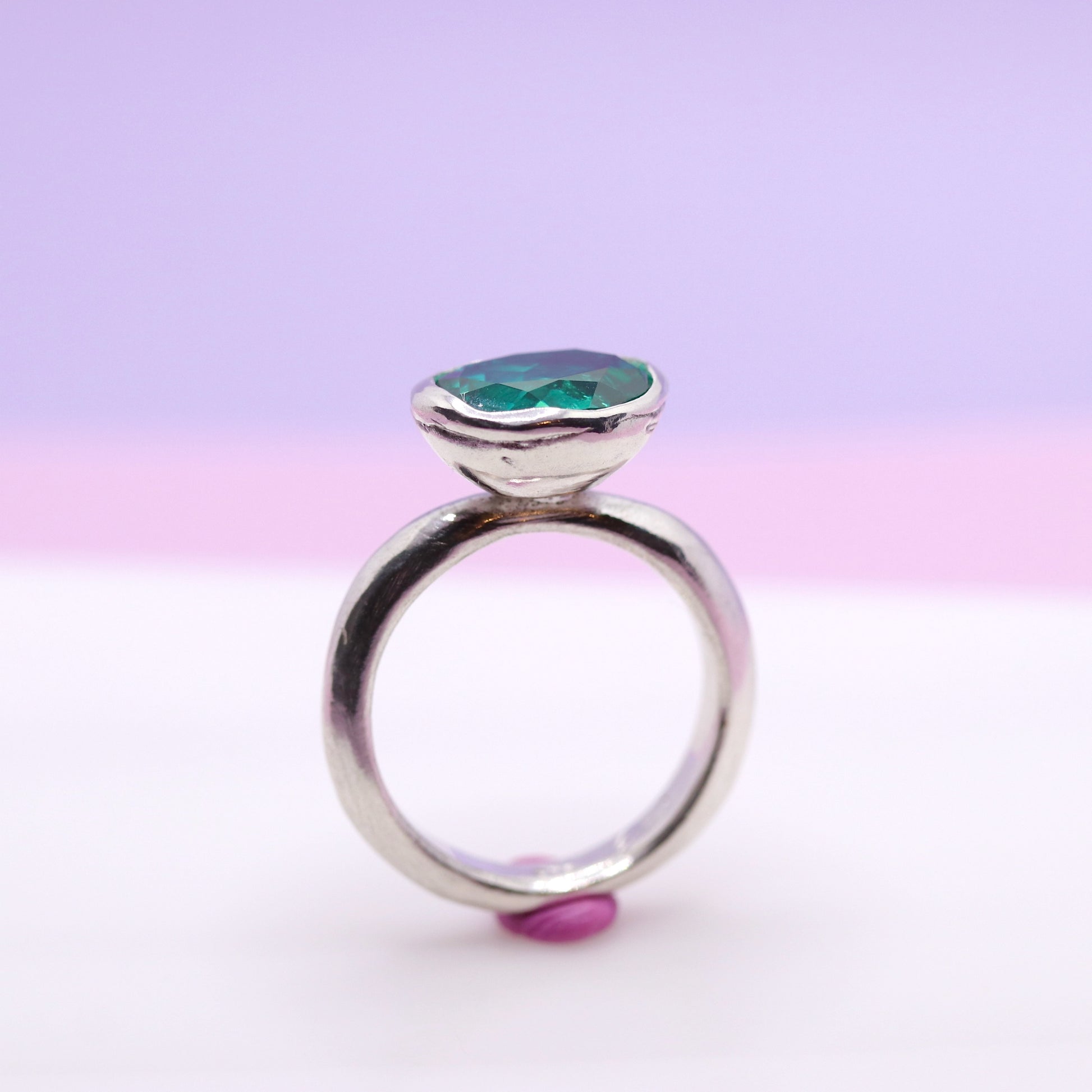 Silver ring with a paraiba green gemstone on a gradient pink and purple background