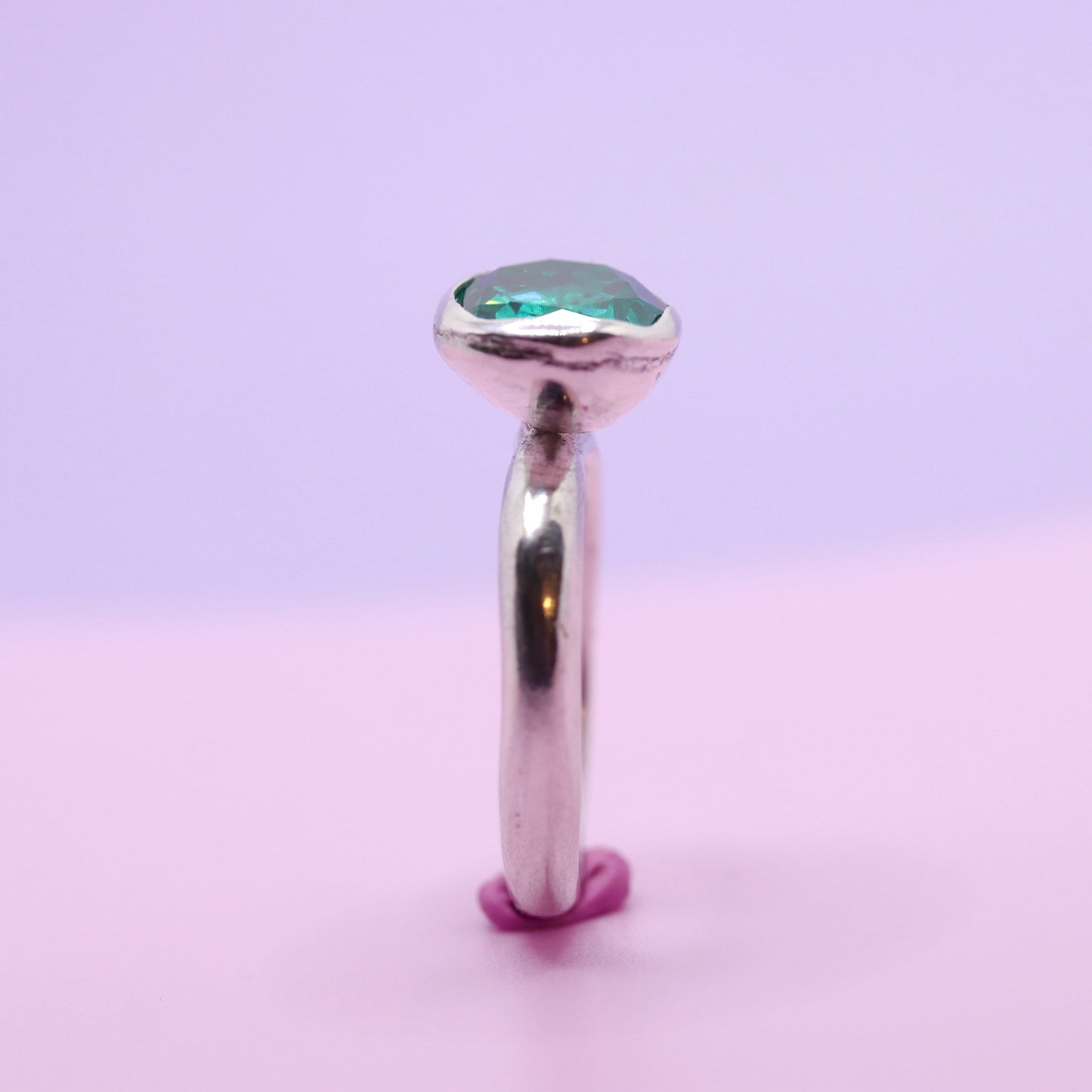 Silver ring with a paraiba green gemstone on a gradient purple and pink background