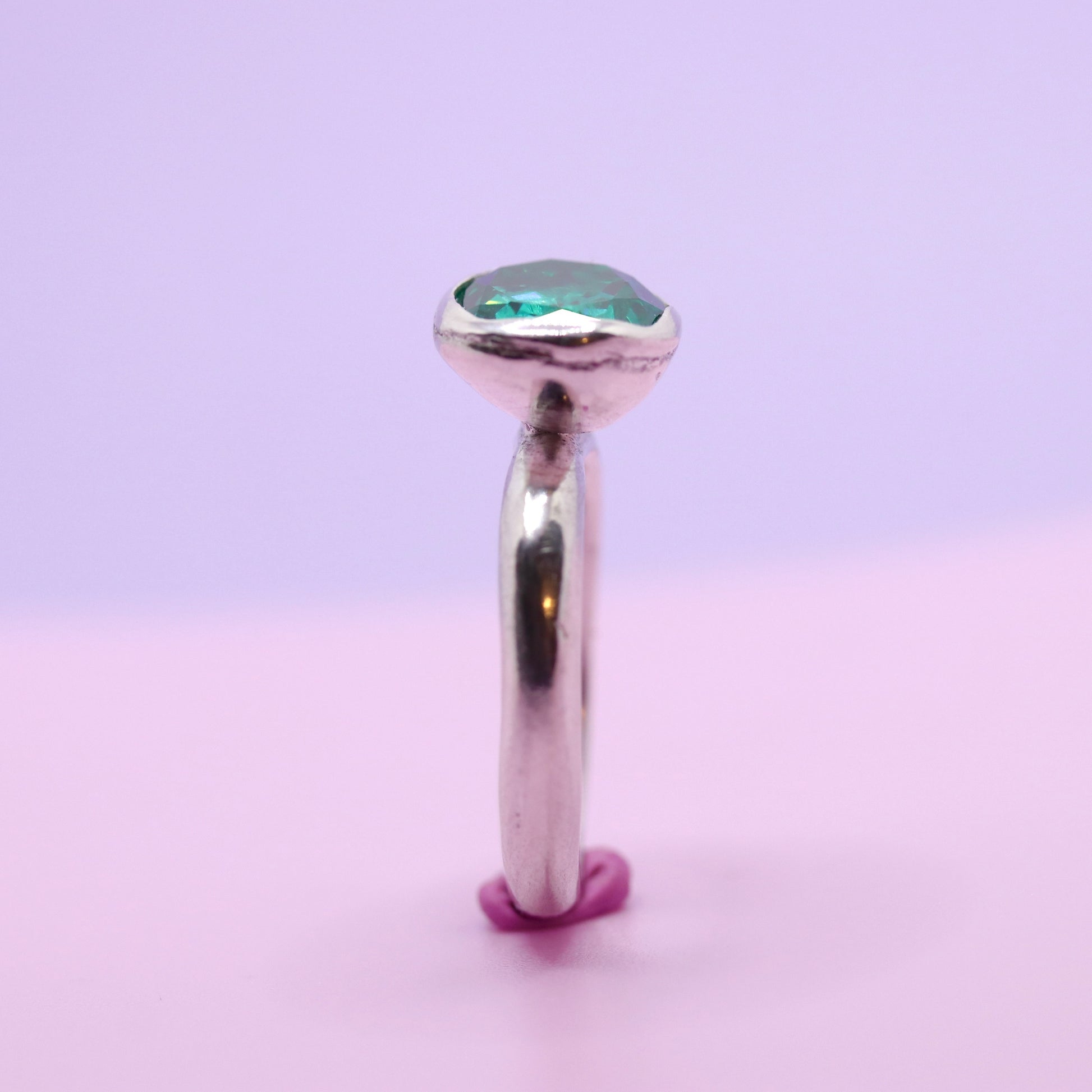 Silver ring with a paraiba green gemstone on a gradient purple and pink background
