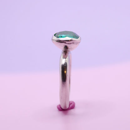 Silver ring with a paraiba green gemstone on a gradient purple and pink background