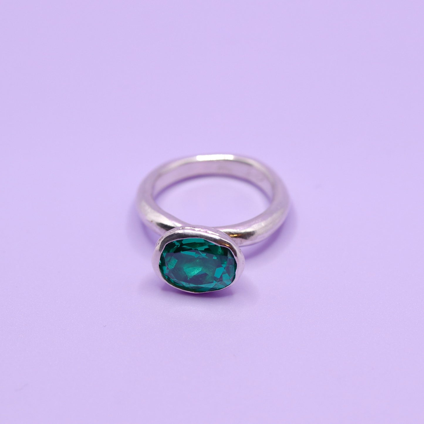 Silver ring with a paraiba green gemstone on a purple background