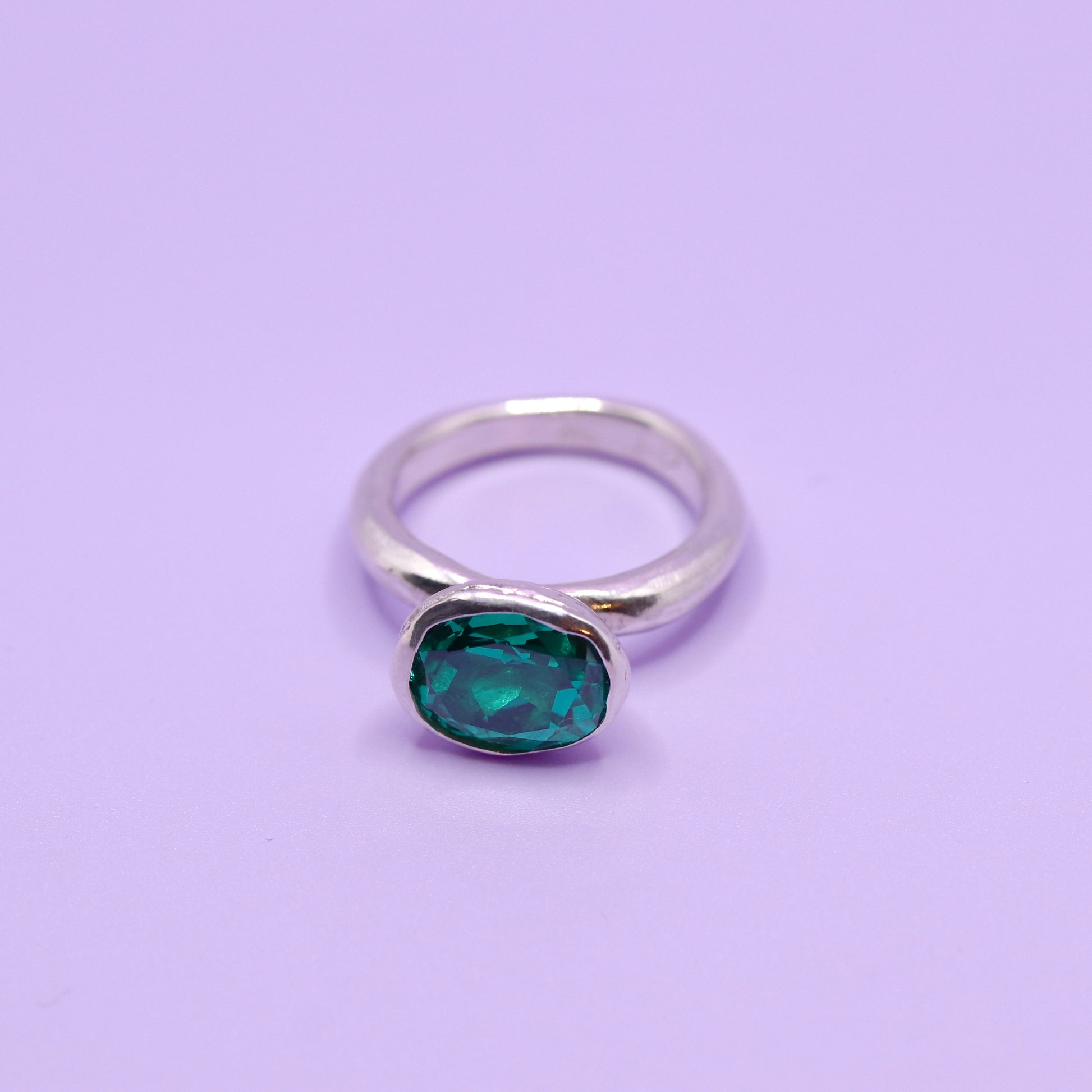 Silver ring with a paraiba green gemstone on a purple background