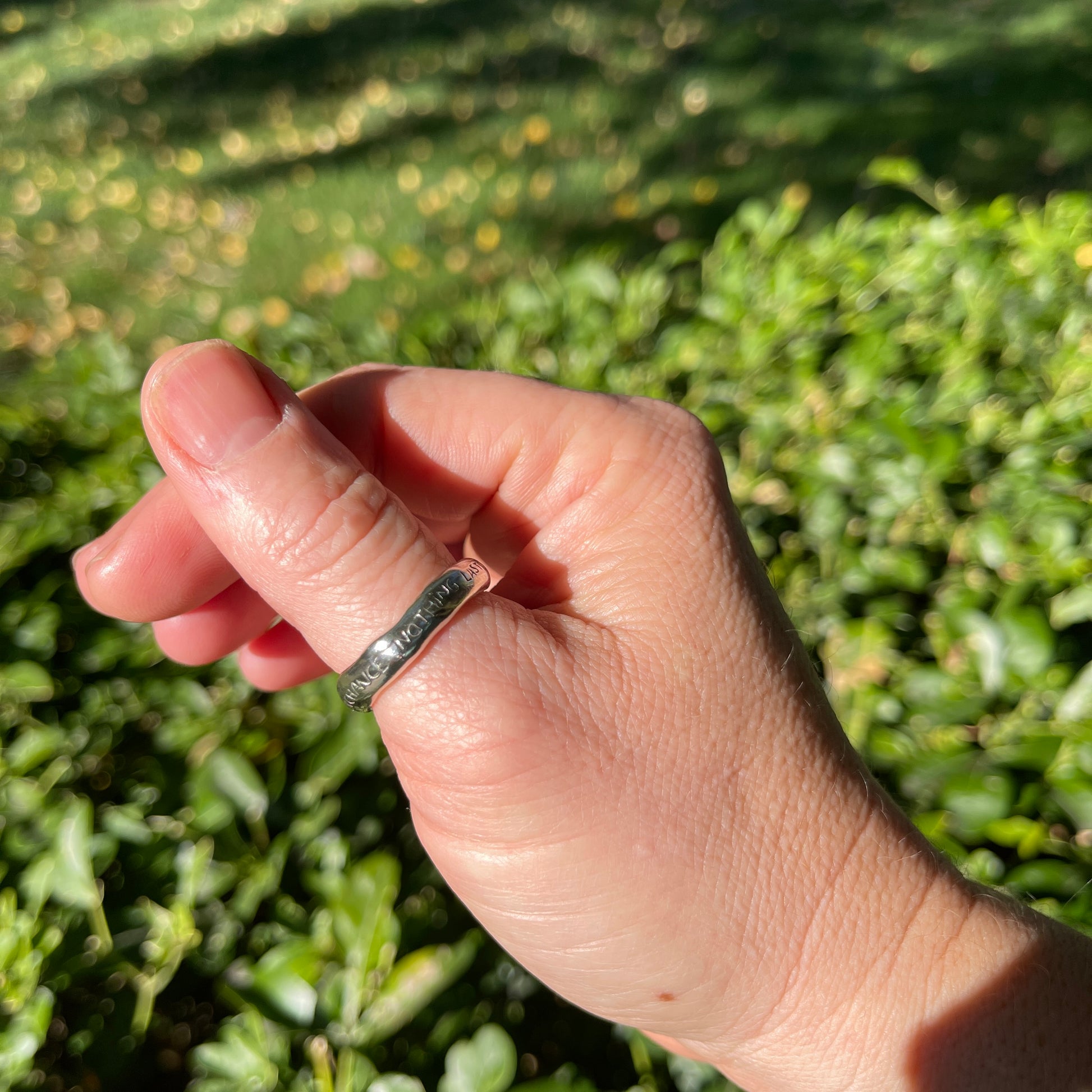 Hand wearing a ring with a green leafy background