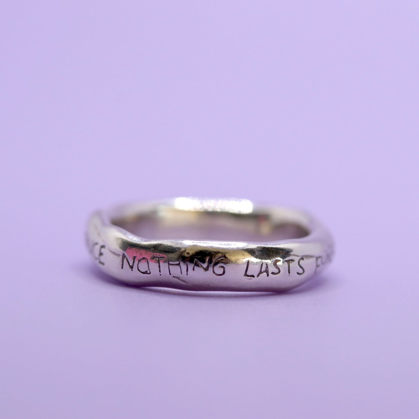 Silver ring with engraved text on a purple background