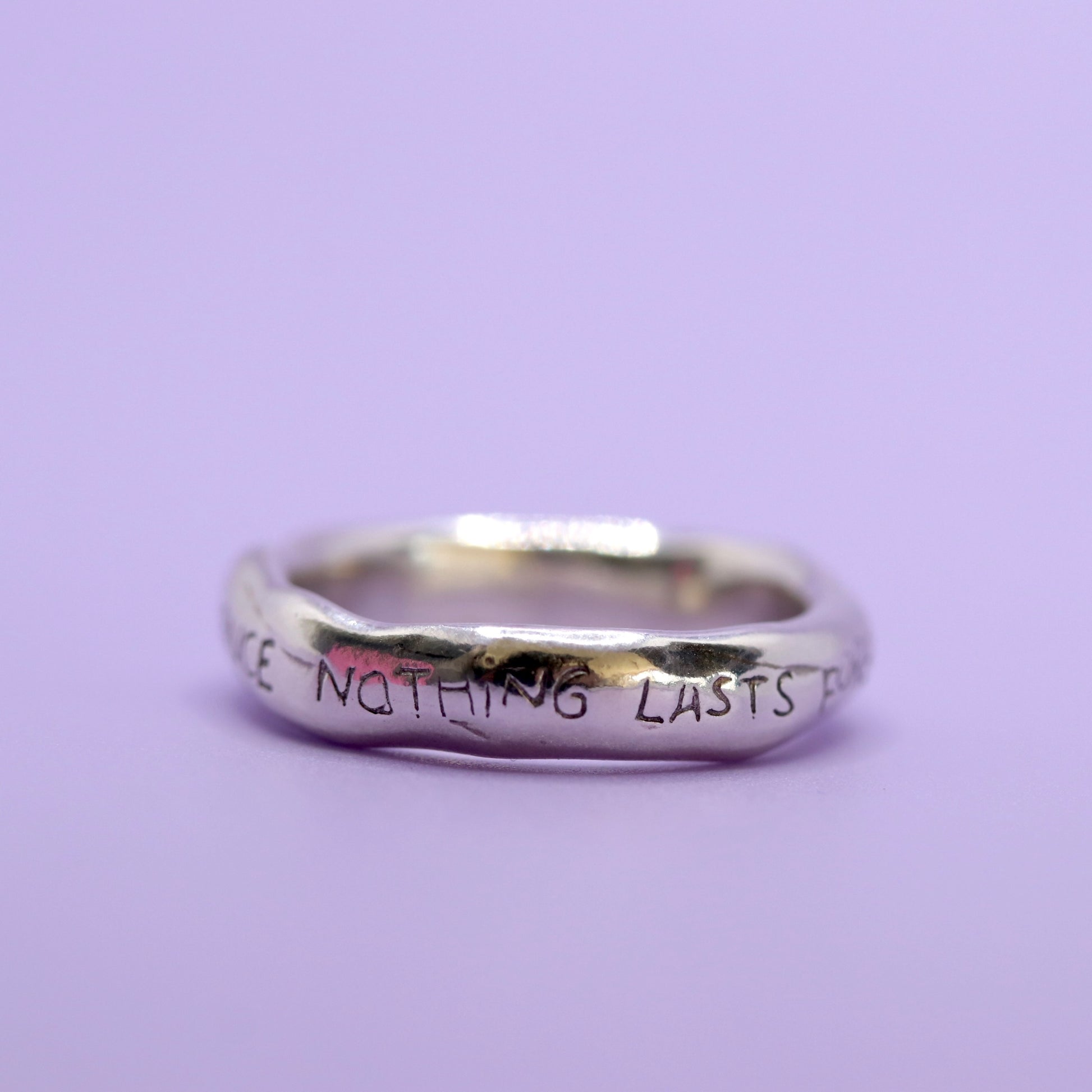 Silver ring with engraved text on a purple background