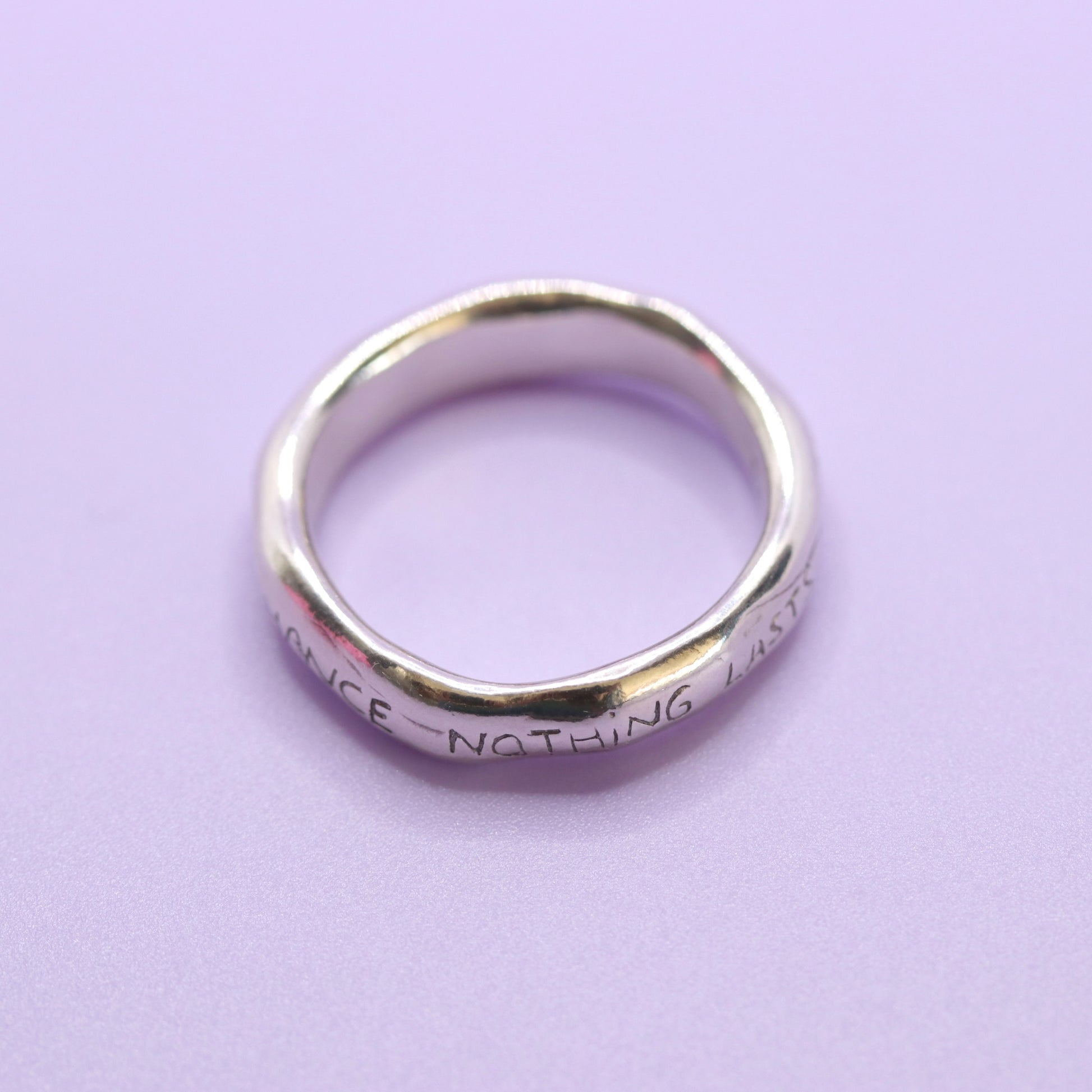Silver ring with engraved text on a purple background