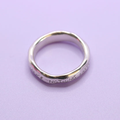 Silver ring with engraved text on a purple background