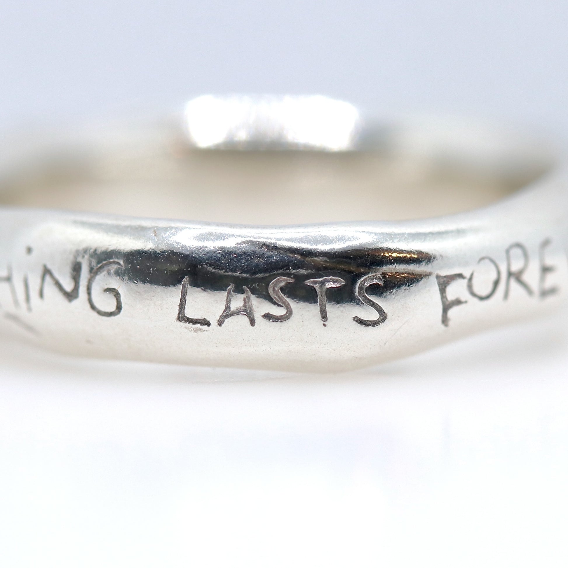 Silver ring with NOTHING LASTS FOREVER' engraved on a white background