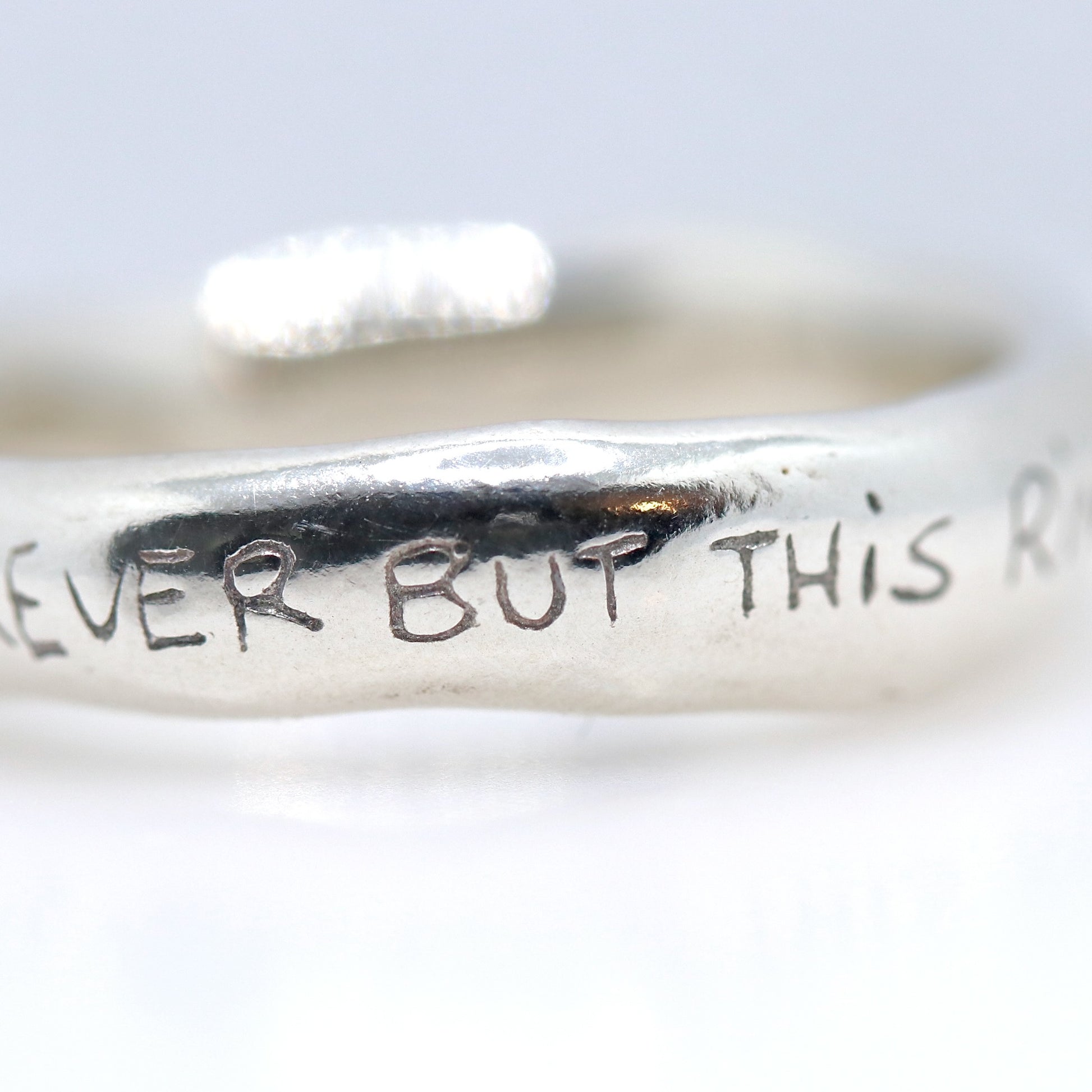 Silver ring with engraved text on a white background