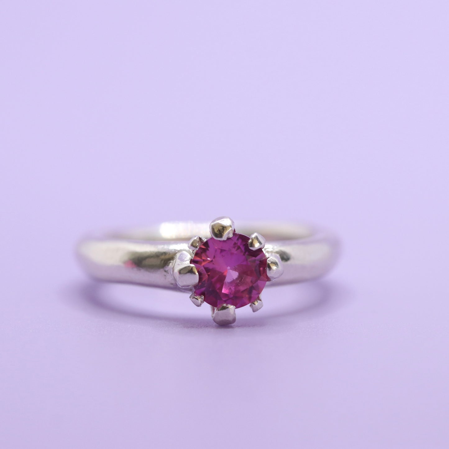 Silver ring with a pink gemstone on a light purple background