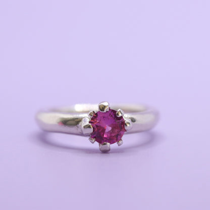 Silver ring with a pink gemstone on a light purple background